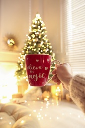 Woman with cup of drink and blurred Christmas tree on background, closeup