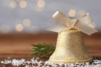Photo of Bell and artificial snow on table against blurred background, closeup with space for text. Christmas decor