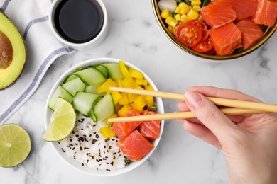 Photo of Woman eating delicious poke bowl with salmon, lime and vegetables on white marble table, top view