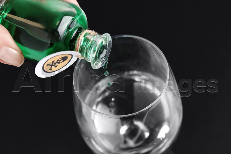 Woman pouring poison into glass of water on black background, closeup