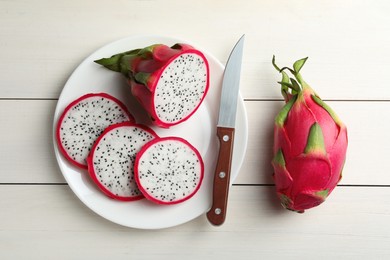 Plate of delicious cut and whole pitahaya fruits with knife on white wooden table, flat lay
