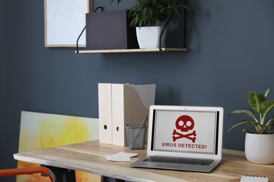 Laptop with warning about virus attack on wooden table in office