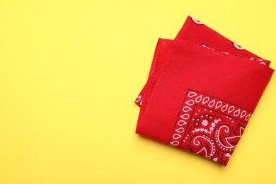Folded red bandana with paisley pattern on yellow background, top view. Space for text