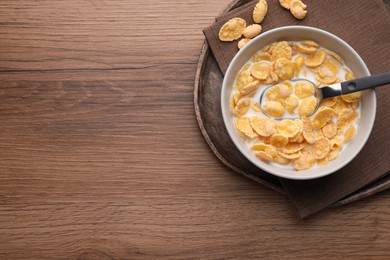 Tasty cornflakes with milk in bowl served on wooden table, top view. Space for text