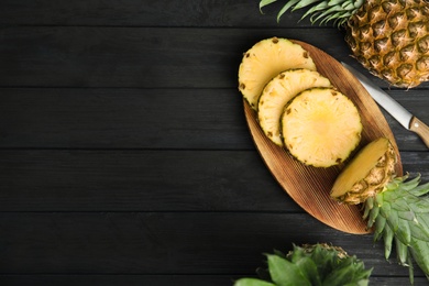 Photo of Whole and cut pineapples on black wooden table, flat lay. Space for text