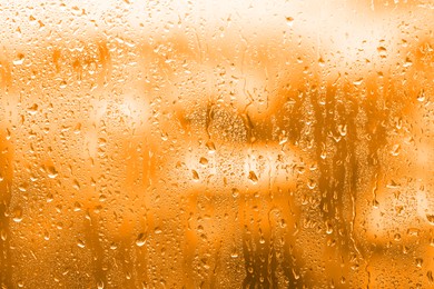 Image of Window glass with raindrops as background, closeup. Toned in orange
