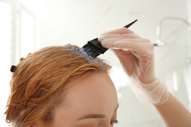 Young woman applying hair dye on roots against light background, closeup