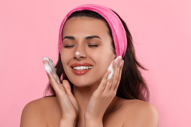 Beautiful woman applying facial cleansing foam on pink background