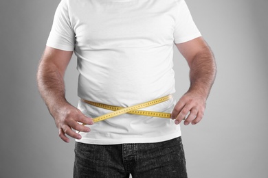 Fat man with measuring tape on grey background, closeup. Weight loss