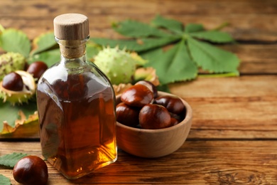 Chestnuts, leaves and bottle of essential oil on wooden table. Space for text