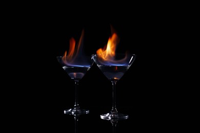 Cocktail glasses with flaming vodka on black background