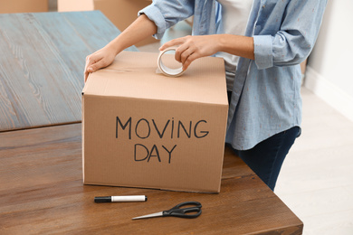 Woman packing box with words MOVING DAY at wooden table, closeup