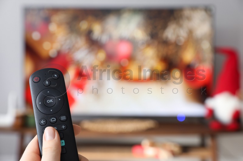 Woman with remote control watching TV at home, closeup. Space for text