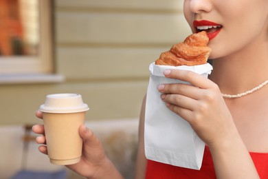 Woman eating croissant and paper cup of coffee outdoors, closeup