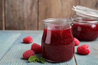 Photo of Delicious jam and fresh raspberries on light blue wooden table