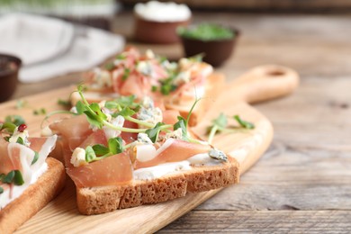 Photo of Delicious sandwiches with prosciutto, cheese and microgreens on wooden table, closeup. Space for text