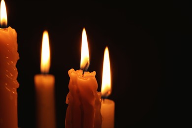 Photo of Burning candles on black background, closeup. Space for text