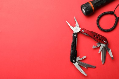 Compact portable multitool, bracelet and flashlight on red background, flat lay. Space for text