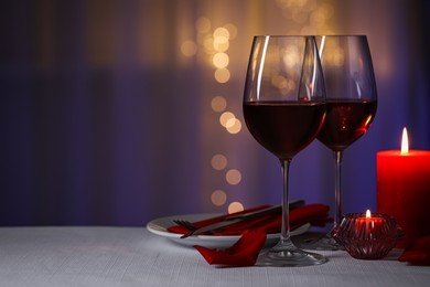 Photo of Romantic table setting with glasses of red wine and burning candles against blurred lights, space for text