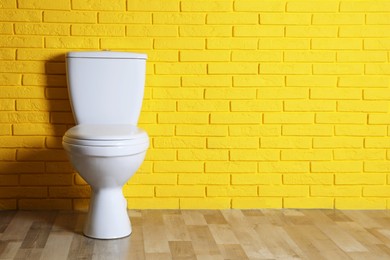 New clean toilet bowl near yellow brick wall indoors, space for text. Interior design