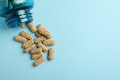 Photo of Overturned bottle with dietary supplement pills on light blue background, flat lay. Space for text