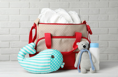 Bag with diapers and baby accessories on wooden table against white brick wall