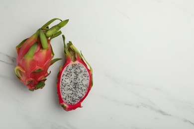 Photo of Delicious cut and whole dragon fruits (pitahaya) on white marble table, flat lay. Space for text