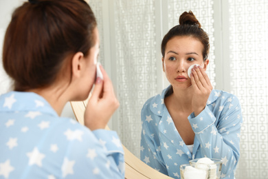 Teen girl with acne problem cleaning her face near mirror in bathroom