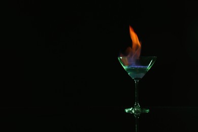 Cocktail glass with flaming vodka on black background, space for text