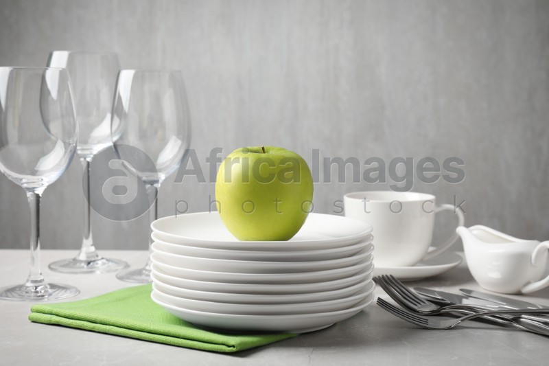 Photo of Clean dishware, glasses, cutlery and apple on light grey table