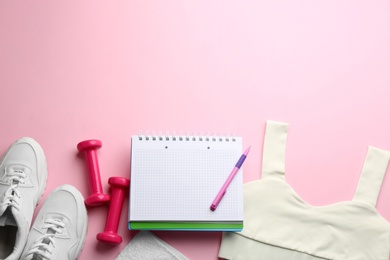 Flat lay composition with sportswear, notebook and dumbbells on pink background, space for text. Gym workout plan