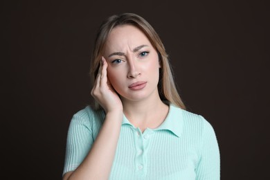Young woman suffering from headache on dark brown background