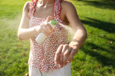 Woman applying insect repellent onto hand in park, closeup