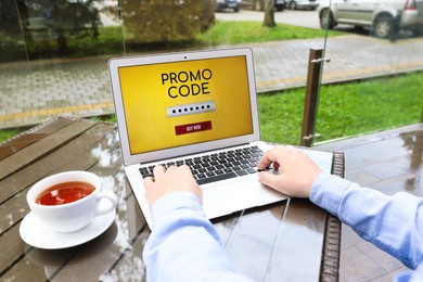 Photo of Man with laptop activating promo code at wooden table outdoors, closeup