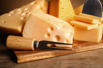 Different sorts of cheese, fork and knife on wooden table, closeup