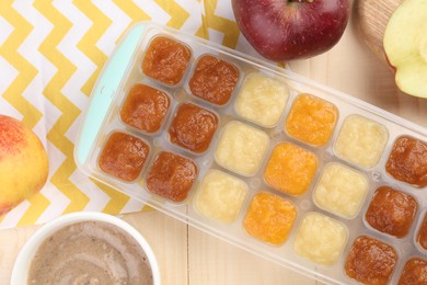 Different purees in ice cube tray and fresh apple fruits on wooden table, flat lay. Ready for freezing