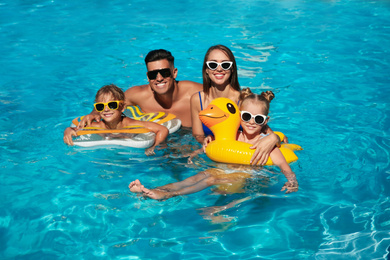 Happy family with inflatable rings in outdoor swimming pool on sunny summer day