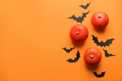 Flat lay composition with pumpkins and paper bats on orange background, space for text. Halloween decor