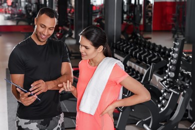 Photo of Happy trainer showing young woman workout plan in modern gym, space for text
