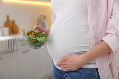 Young pregnant woman with vegetable salad in kitchen, closeup. Healthy eating
