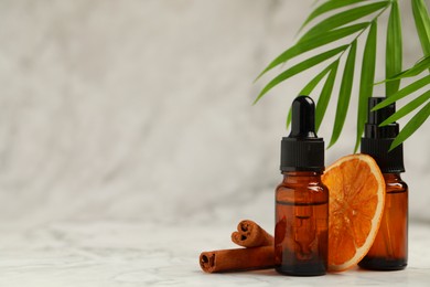 Photo of Bottles of organic cosmetic products, cinnamon sticks, dried orange slice and green leaves on light marbled background, space for text