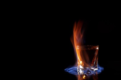Glass with flaming vodka on black background, space for text