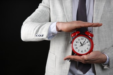 Businessman holding alarm clock on black background, closeup. Time management