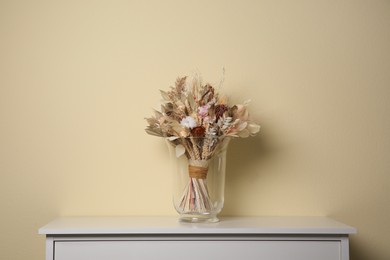 Beautiful dried flower bouquet in glass vase on white table near beige wall