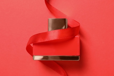 Bottle of perfume with ribbon on red background, top view