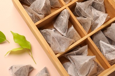 Photo of Many tea bags in wooden box and leaves on color background, closeup