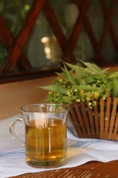 Photo of Glass cup of aromatic tea and linden blossoms on wooden table, space for text