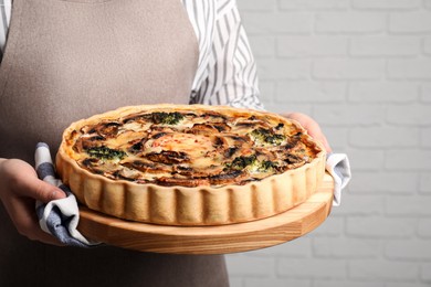 Photo of Woman holding delicious homemade quiche with mushrooms near white brick wall, closeup