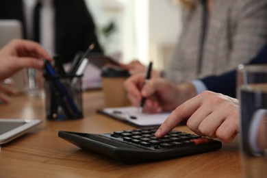 Man using calculator at table in office during business meeting, closeup. Management consulting