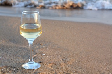 Photo of Glass of tasty wine on sand near sea, space for text